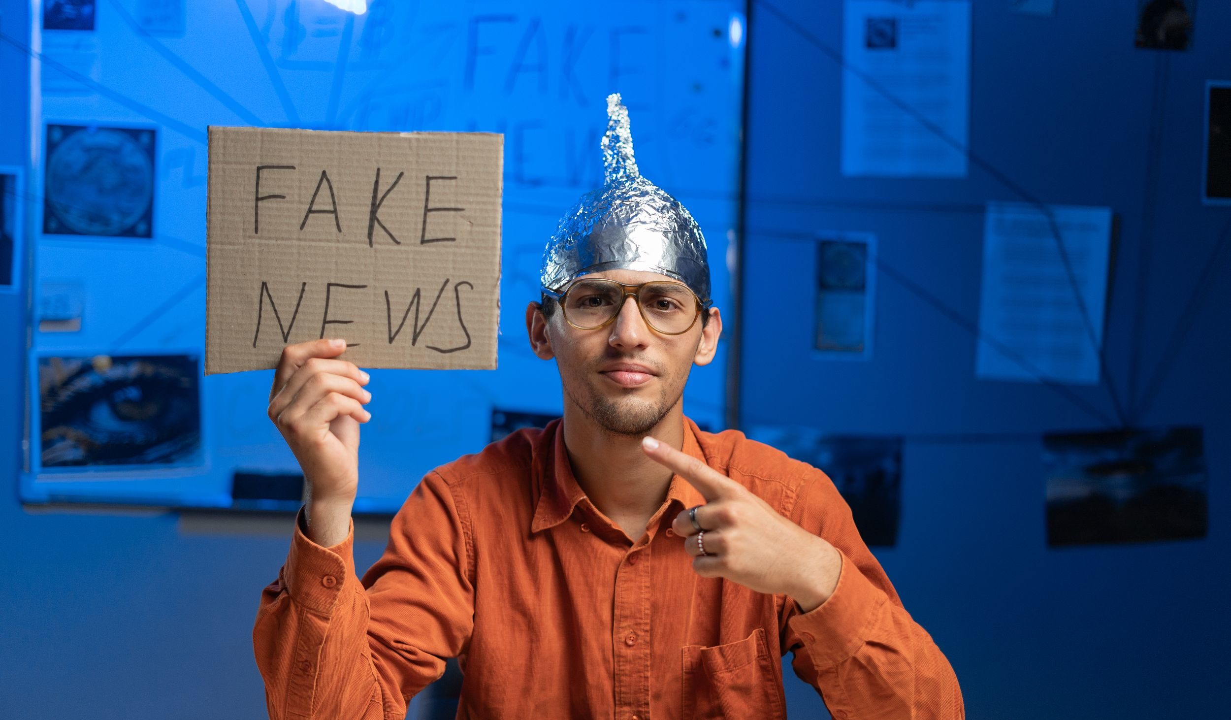 Male conspiracy theorist in a protective foil cap and glasses debunks myths holding poster fake news. Conspiracy theory concept. The schizophrenic works.