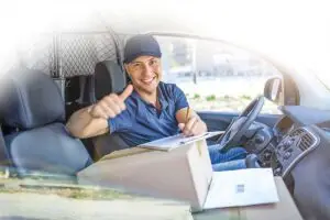 Junger Mann sitzt mit Paket im Lieferwagen