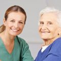 Altenpflege durch lächelnde Krankenschwester bei einer glücklichen Seniorin