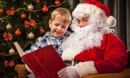 Santa Claus and a little boy reading together a book or list in front of Christmas Tree